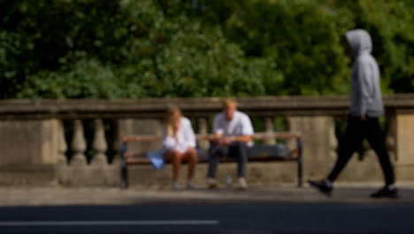 Defocused-Shot-of-People-and-Traffic-Moving-In-Front-of-Couple-Sat-On-Bench-02