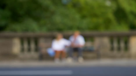Defocused-Shot-of-Traffic-and-People-Moving-In-Front-of-Couple-Sat-On-Bench-01