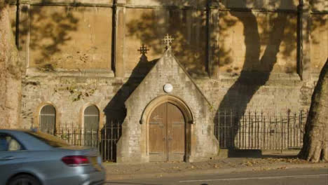 Wide-Shot-of-Car-and-Cyclist-Passing-Past-Doors-to-St-Nicholas-Church-In-Bristol-