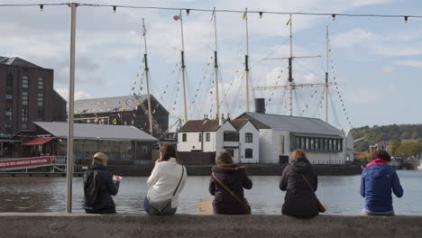 Tracking-Shot-Approaching-People-Sitting-On-Waterfront-at-Bristol-Harbour-