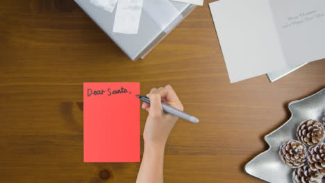 Top-Down-View-of-Hand-Writing-Dear-Santa-On-Paper-with-Presents-and-Cards