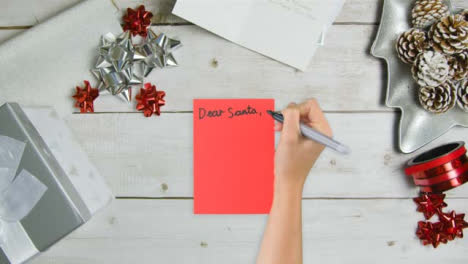 Top-Down-View-of-Hand-Writing-Dear-Santa-On-Paper-with-Christmas-Gifts-and-Cards