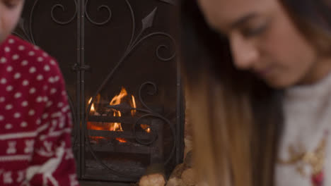Sliding-Shot-of-Burning-Fireplace-Behind-Young-Couple-Wrapping-Christmas-Presents