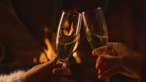 Close-Up-of-Two-People-Bringing-Their-Champagne-Glasses-Together-In-Front-of-Burning-Fire