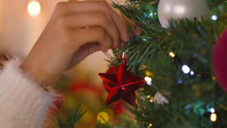 Extreme-Close-Up-of-Female-Hand-Placing-Decoration-On-Christmas-Tree