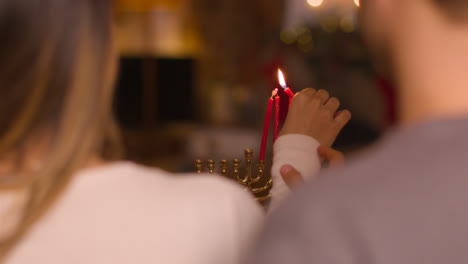 Over-the-Shoulder-Shot-of-Young-Couple-Lighting-Candles-of-Menorah-During-Hanukkah