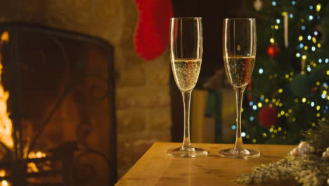 Sliding-Close-Up-of-Two-Glasses-of-Champagne-On-Table-In-Front-of-Fireplace