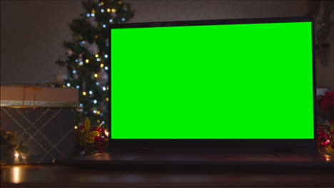 Close-Up-Shot-of-Laptop-Green-Screen-On-Table-In-Front-of-Christmas-Themed-Backdrop