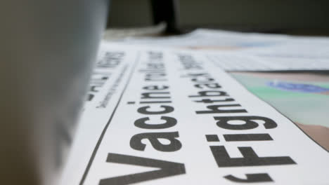 Sliding-Extreme-Close-Up-of-Pile-of-Newspapers-with-Headlines-On-Covid-19-Vaccines