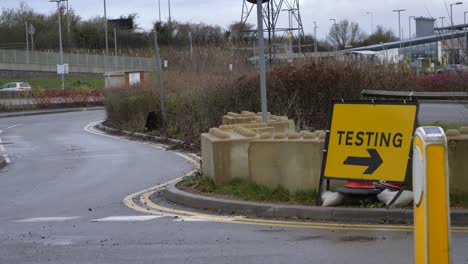 Handheld-Wide-Shot-of-Car-Driving-Past-COVID-Test-Site-Road-Sign
