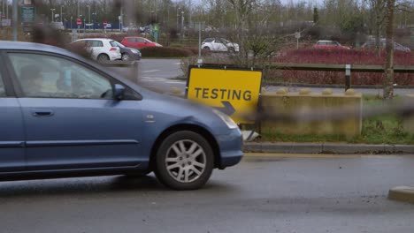 Handheld-Pull-Focus-Shot-of-Car-Driving-Past-COVID-19-Test-Site-Road-Sign