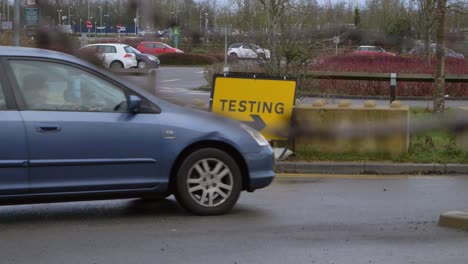 Handheld-Pull-Fokus-Aufnahme-Des-Autos,-Das-Am-Straßenschild-Des-Covid-19-Testgeländes-Vorbeifährt