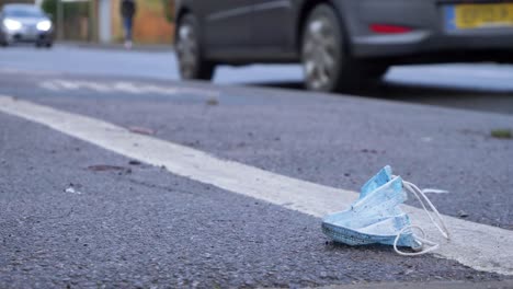 Close-Up-of-a-Discarded-Face-Mask-On-Floor-with-Cars-and-Pedestrians-In-Background