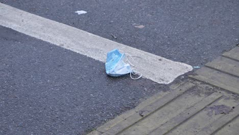 Handheld-High-Angle-Shot-of-a-Discarded-Face-Mask-On-Pavement