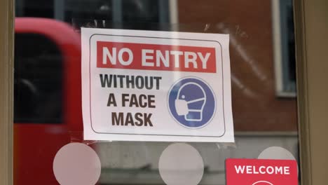Handheld-Close-Up-Shot-of-COVID-19-Face-Mask-Sign-In-a-Shop-Window