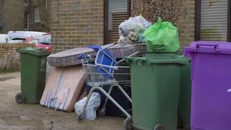 Handheld-Medium-Shot-of-Trolley-and-Mattresses-Dumped-By-Bins-