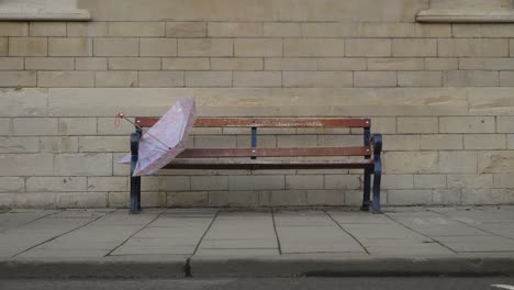 Wide-Shot-of-Discarded-Umbrella-On-Bench-as-People-Walk-Past