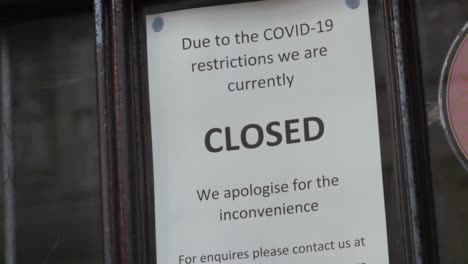 Handheld-Close-Up-Shot-of-Closure-Sign-In-Shop-Window-During-COVID-Pandemic