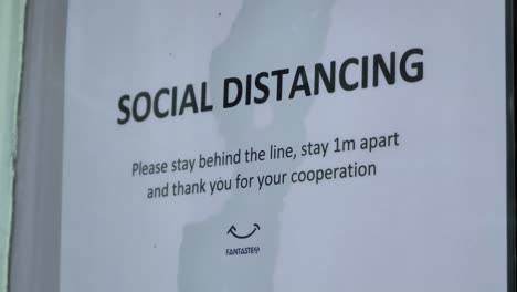 Handheld-Close-Up-Shot-of-Social-Distancing-Sign-In-Shop-Window-During-COVID-19-Pandemic