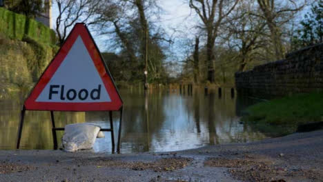 Close-Up-Shot-of-Flood-Road-Sign-In-Front-of-a-Flooded-Road