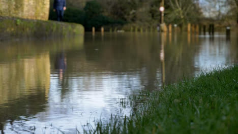 Defocused-Shot-of-Pedestrian-Walking-Along-High-Path-Next-to-Flooded-Road