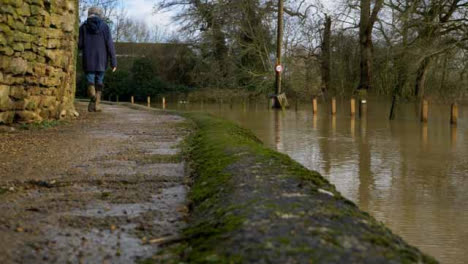 Wide-Shot-of-Person-Walking-Along-High-Path-Next-to-Flooded-Road