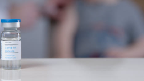 Sliding-Close-Up-Shot-of-Doctors-Hand-Picking-Up-COVID-Vaccine-Vials-Before-Injection-Background-Child-Patient