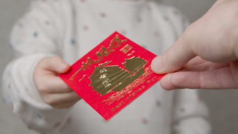 Close-Up-Shot-of-Hand-Giving-Chinese-New-Year-Red-Envelope-to-Child