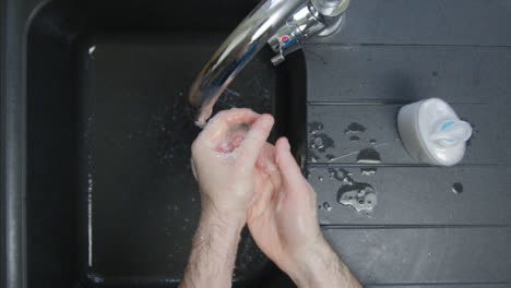 Top-Down-Shot-of-Male-Hands-Washing-with-Soap-Under-Running-Tap