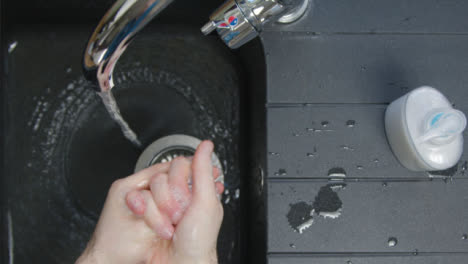 Top-Down-Shot-of-Male-Hands-Turning-Washing-Underneath-Running-Tap