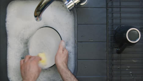 Top-Down-Shot-of-Male-Hands-Washing-Plate-In-Sink-of-Soapy-Water