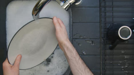 Von-Oben-Nach-Unten-Geschossen-Von-Männlichen-Händen,-Die-Teller-In-Einem-Waschbecken-Mit-Seifenwasser-Waschen-Washing