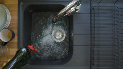 Top-Down-Shot-of-Male-Hands-Pouring-Washing-Liquid-into-Sink-Under-a-Running-Tap