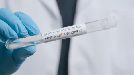 Close-Up-Shot-of-Doctor-Walking-Towards-Camera-Holding-Positive-COVID-Test-Tube-In-Hand