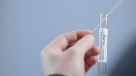 Over-the-Shoulder-Shot-of-Person-Placing-Used-Swab-In-Test-Tube-During-Home-COVID-Self-Test