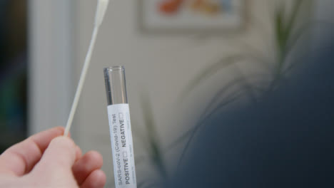 Over-the-Shoulder-Shot-of-Person-Placing-a-Used-Swab-In-Test-Tube-During-Home-COVID-Self-Test