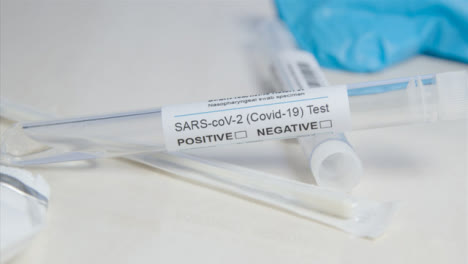Sliding-Close-Up-of-COVID-Test-Tube-and-Swab-On-Table-Surface