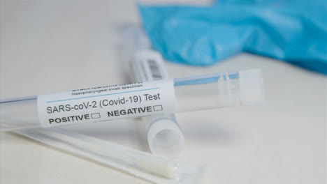 Sliding-Close-Up-of-COVID-Test-Tube-and-Swab-On-a-Table-Surface
