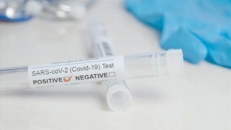 Sliding-Close-Up-of-COVID-Positive-Test-Tube-and-Swab-On-a-Table-Surface