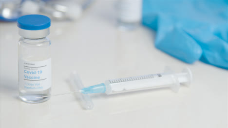 Sliding-Close-Up-of-COVID-Vaccine-Vial-and-Syringe-On-Table-Surface