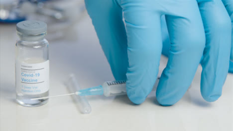 Sliding-Close-Up-of-Doctors-Hand-Picking-Up-COVID-Vaccine-Vial-and-Syringe-from-Table