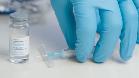 Sliding-Close-Up-of-Doctors-Hand-Picking-Up-COVID-Vaccine-Vial-and-Syringe-from-Table-