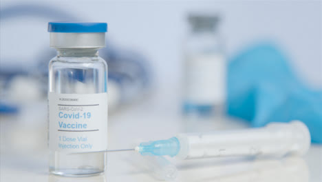 Sliding-Close-Up-of-COVID-a-Vaccine-Vial-and-Syringe-On-Table-Surface