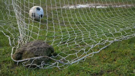 Close-Up-Shot-of-Rock-Holding-Down-Goal-Net-as-Soccer-Ball-Lands-In-Front-of-It