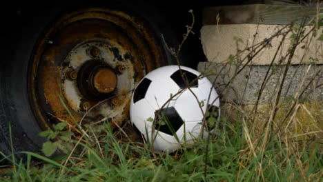 Close-Up-Shot-of-Soccer-Ball-Landing-Next-Rusted-Wheel-and-Concrete-Blocks