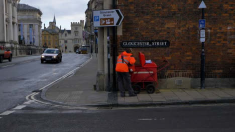 Tracking-Shot-Past-Postal-Worker-On-Street-Corner-as-Traffic-Drives-Past-