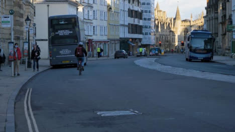 Handheld-Wide-Shot-of-Cyclist-Riding-Down-Street-Past-Bus-