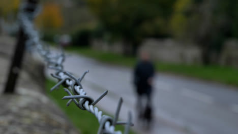 Close-Up-Shot-of-Barbed-Wire-Fence-with-Dog-Walker-In-Background