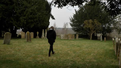 Wide-Shot-of-Young-Woman-Walking-Through-Rural-Graveyard-