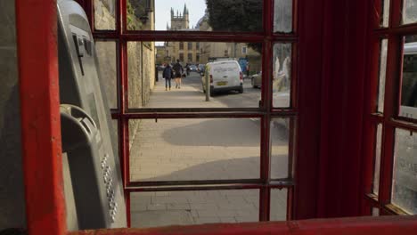 Wide-Shot-Looking-Through-Disused-Phone-Box-at-People-Walking-Down-Street